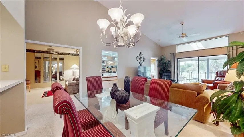 Carpeted dining room featuring high vaulted ceiling and ceiling fan with notable chandelier