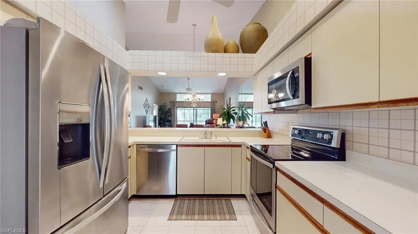 Kitchen featuring decorative light fixtures, stainless steel appliances, backsplash, sink, and light tile floors