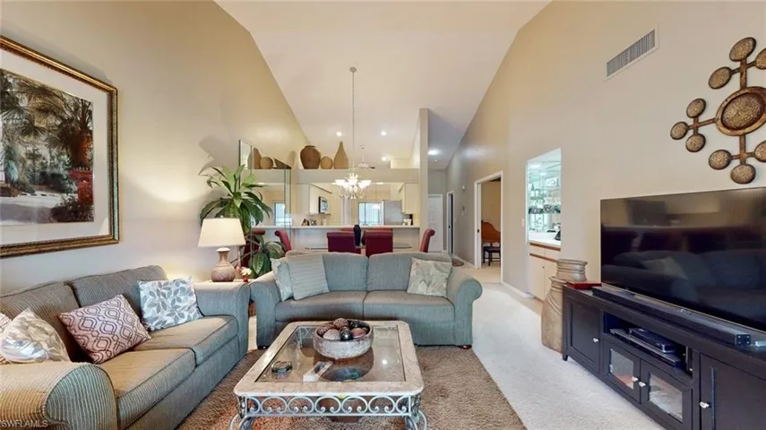 Carpeted living room featuring high vaulted ceiling and an inviting chandelier