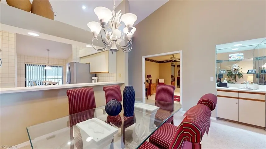 Dining space with high vaulted ceiling, sink, light colored carpet, and ceiling fan with notable chandelier