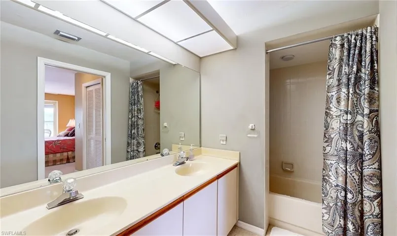 Bathroom featuring dual sinks, shower / bath combination with curtain, and vanity with extensive cabinet space