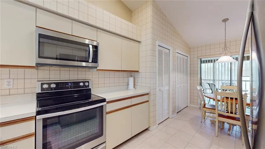 Kitchen featuring stainless steel appliances, backsplash, light tile floors, hanging light fixtures, and lofted ceiling