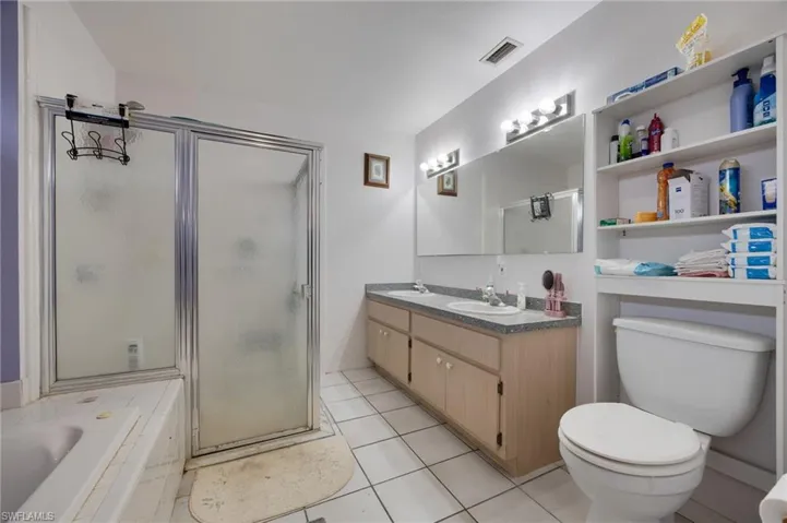 Bathroom featuring a stall shower, double vanity, light tile patterned flooring, and tiled bath