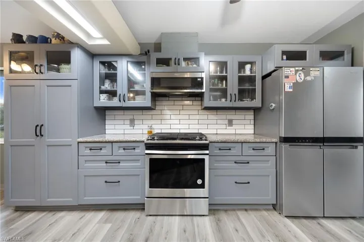 Kitchen with gray cabinets, stainless steel appliances, backsplash, and light stone counters