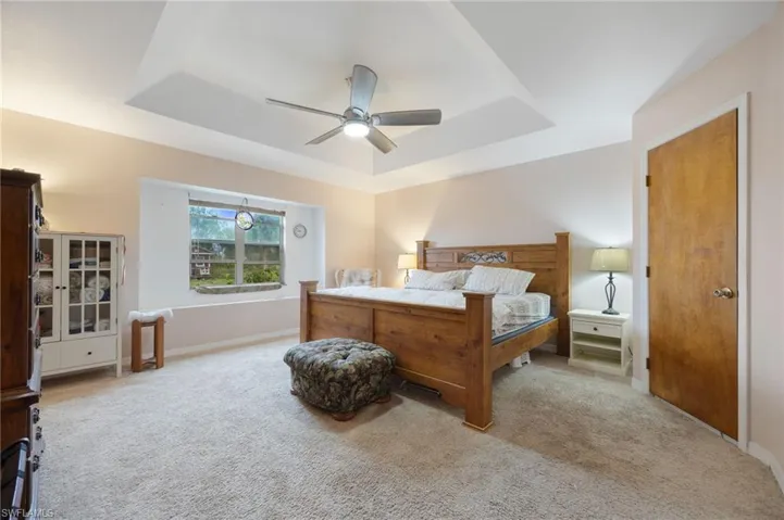 Bedroom featuring light carpet, a tray ceiling, and ceiling fan