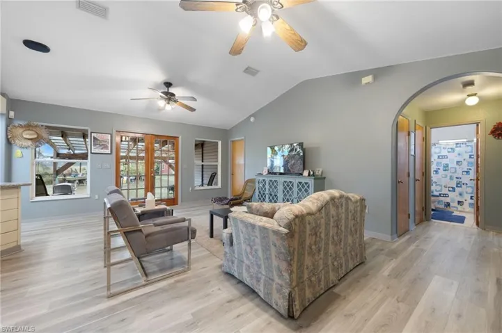 Living area with vaulted ceiling, light wood-style flooring, french doors, a ceiling fan, and arched walkways