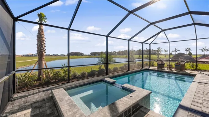 View of pool with glass enclosure, a water view, a pool with connected hot tub, and a patio area
