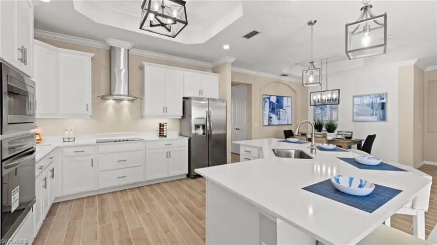 Kitchen with stainless steel appliances, a chandelier, a sink, visible vents, and wall chimney range hood