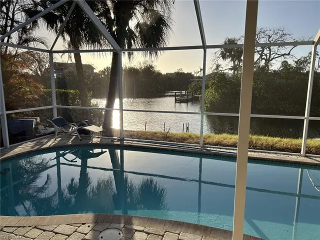 Pool at dusk featuring a water view and glass enclosure