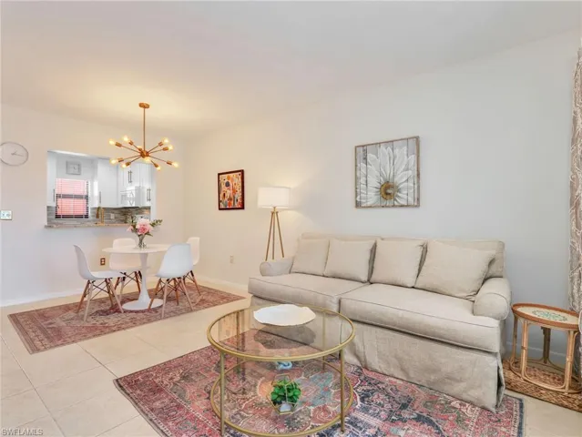 Open-concept interior featuring light tile flooring, neutral wall paint, a multi-arm modern brass chandelier, and a breakfast bar passthrough