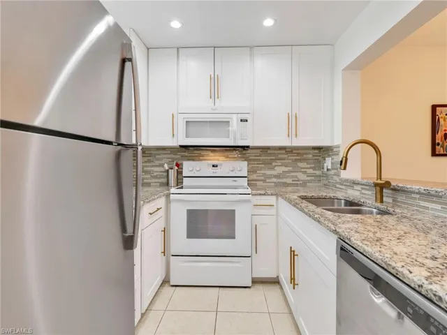 Kitchen featuring white cabinetry with gold-tone pulls, stone-finish countertops, stainless steel appliances, a multi-tonal tile backsplash, and a gooseneck faucet