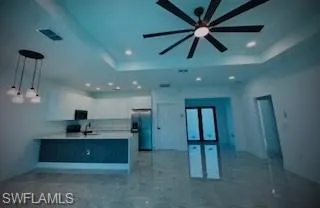 Kitchen featuring a raised ceiling, open floor plan, a peninsula, light countertops, and recessed lighting