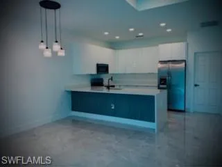 Kitchen with stainless steel refrigerator with ice dispenser, light countertops, white cabinetry, decorative light fixtures, and a peninsula