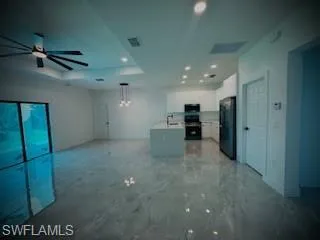 Unfurnished living room featuring a raised ceiling, recessed lighting, a ceiling fan, and light marble finish floors