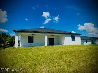 Back of property featuring stucco siding, a ceiling fan, and a lawn