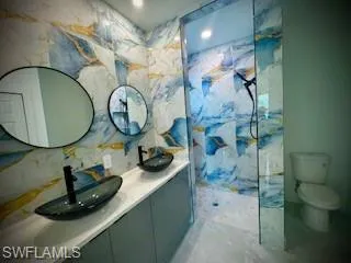 Full bathroom with vanity, a marble finish shower, tile walls, and light marble finish floors