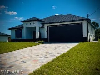 View of front of house with a garage, decorative driveway, a front lawn, and stucco siding