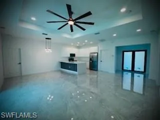 Unfurnished living room featuring a raised ceiling, a ceiling fan, recessed lighting, and light marble finish floors