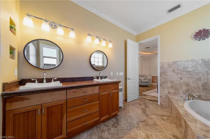 Bathroom with vanity, crown molding, and tiled bath