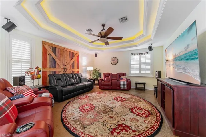 Living room with ceiling fan, a raised ceiling, and crown molding