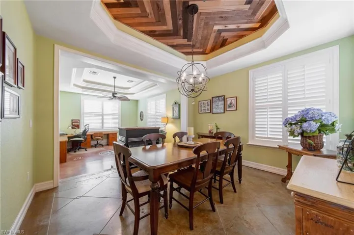 Dining space with ceiling fan with notable chandelier, a raised ceiling, and ornamental molding