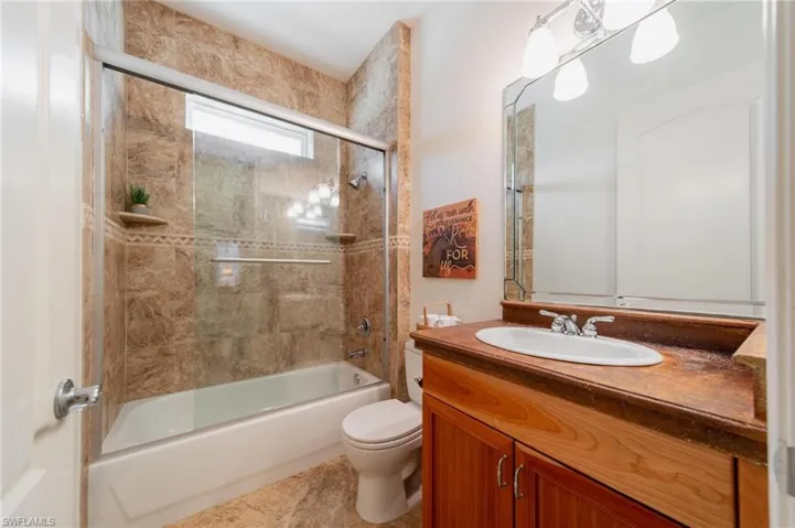 Full bathroom with tile patterned flooring, vanity, enclosed tub / shower combo, and toilet