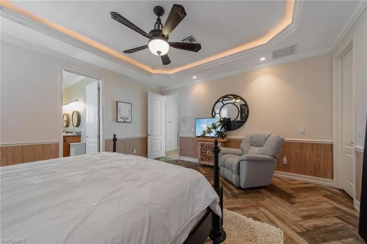 Bedroom featuring parquet flooring, ensuite bathroom, ornamental molding, a tray ceiling, and ceiling fan