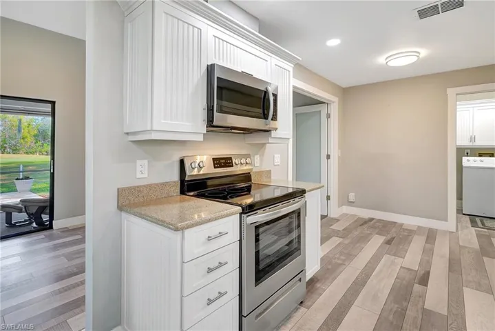 Kitchen with white cabinets, appliances with stainless steel finishes, light hardwood / wood-style floors, and light stone countertops