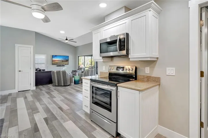 Kitchen featuring appliances with stainless steel finishes, ceiling fan, light hardwood / wood-style floors, white cabinetry, and lofted ceiling