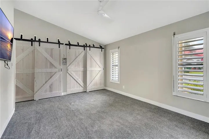 Unfurnished room with a barn door, ceiling fan, carpet floors, and lofted ceiling