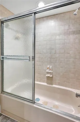 Bathroom with combined bath / shower with glass door and wood-type flooring