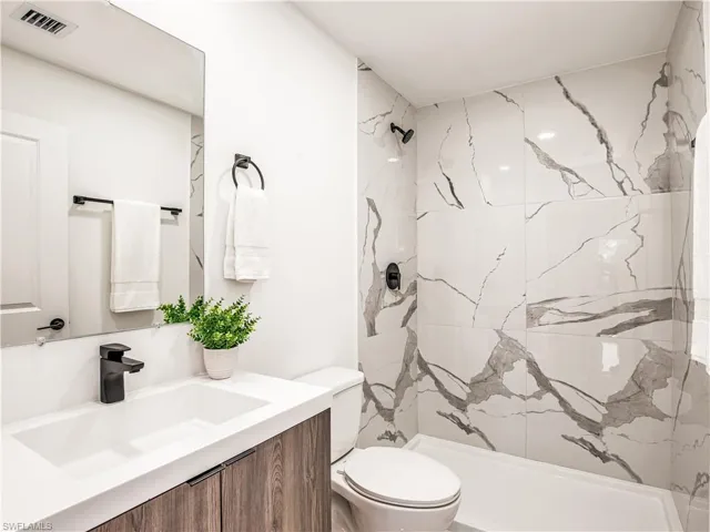 Bathroom featuring toilet, a marble style finish shower, and vanity