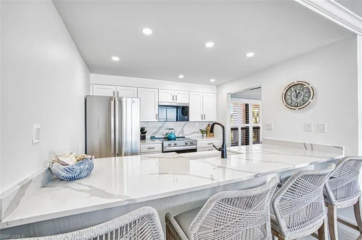 Kitchen with a peninsula, a breakfast bar, stainless steel appliances, light quartz counters, and white cabinetry
