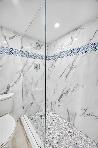 Bathroom with a marble finish shower, recessed lighting, and tile walls