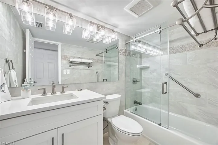 Full bathroom with tile walls, vanity, and bath / shower combo with glass door