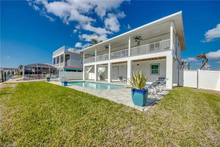 Rear view of property featuring a patio area, a balcony, a lawn, ceiling fan, and a fenced in pool