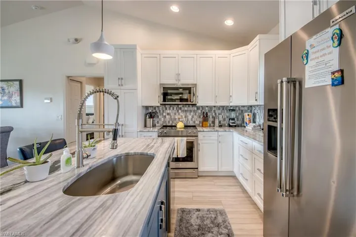Kitchen featuring sink, hanging light fixtures, stainless steel appliances, light stone countertops, and white cabinets