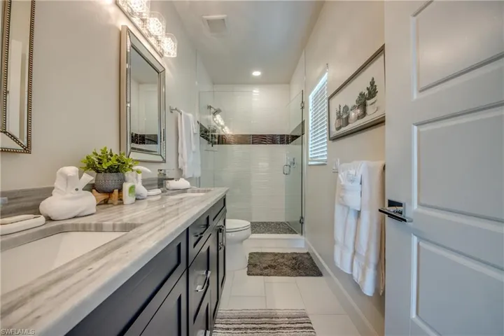 Bathroom with tile patterned floors, vanity, toilet, and a shower with door