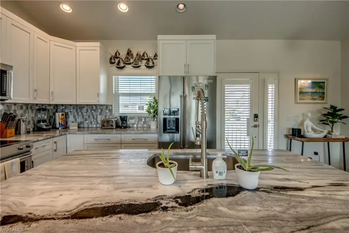 Kitchen featuring light stone counters, tasteful backsplash, white cabinets, and appliances with stainless steel finishes