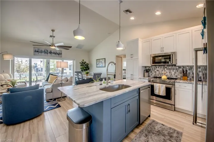 Kitchen with stainless steel appliances, white cabinetry, hanging light fixtures, and sink