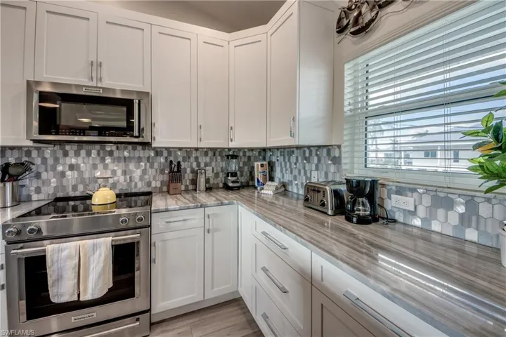Kitchen with stainless steel appliances, light stone countertops, white cabinets, and decorative backsplash