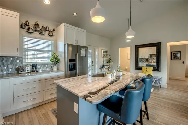 Kitchen with appliances with stainless steel finishes, decorative light fixtures, white cabinetry, light stone countertops, and a center island with sink