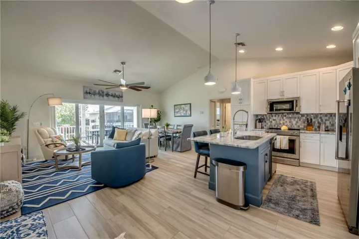Kitchen featuring pendant lighting, appliances with stainless steel finishes, a kitchen island with sink, white cabinetry, and light stone counters