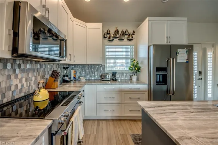 Kitchen with white cabinetry, decorative backsplash, light hardwood / wood-style floors, light stone counters, and stainless steel appliances
