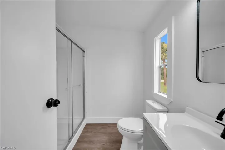 Bathroom featuring a glass-enclosed shower, wood-finish flooring, a contemporary vanity with an integrated sink, and a framed mirror