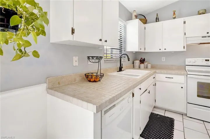 Kitchen featuring white appliances, light tile patterned floors, tile counters, sink, and white cabinets