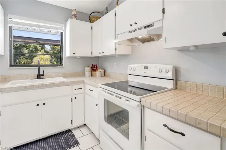 Kitchen featuring white cabinetry, tile countertops, light tile patterned floors, sink, and electric range