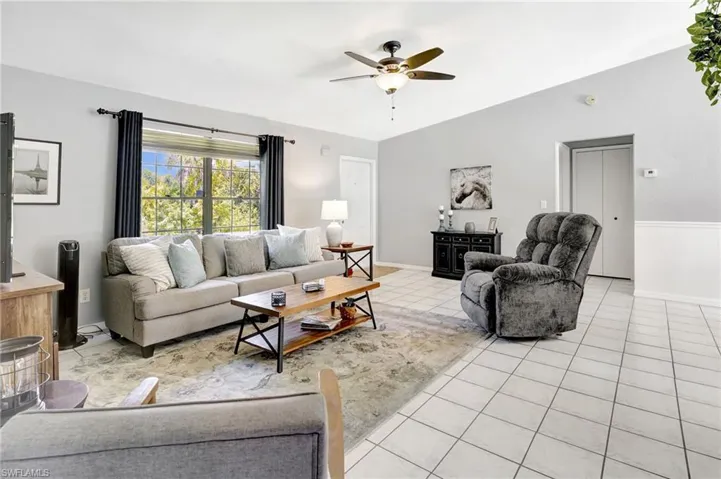 Living room with ceiling fan, light tile patterned floors, and vaulted ceiling