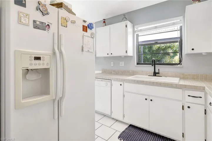 Kitchen with white appliances, white cabinetry, sink, light tile patterned flooring, and tile counters