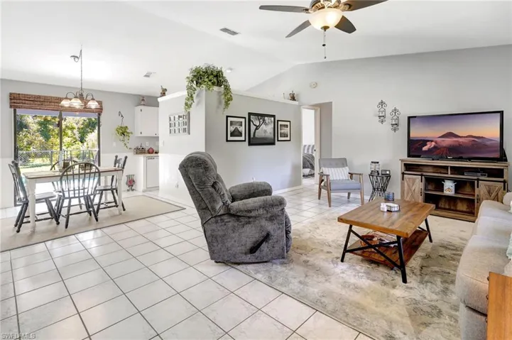 Living room featuring vaulted ceiling, ceiling fan with notable chandelier, and light tile patterned flooring
